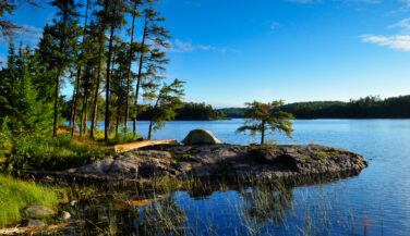 BWCA Landscape-Scott Poska, 2020. A canoe on a rock by some trees by the lake in the Boundary Waters